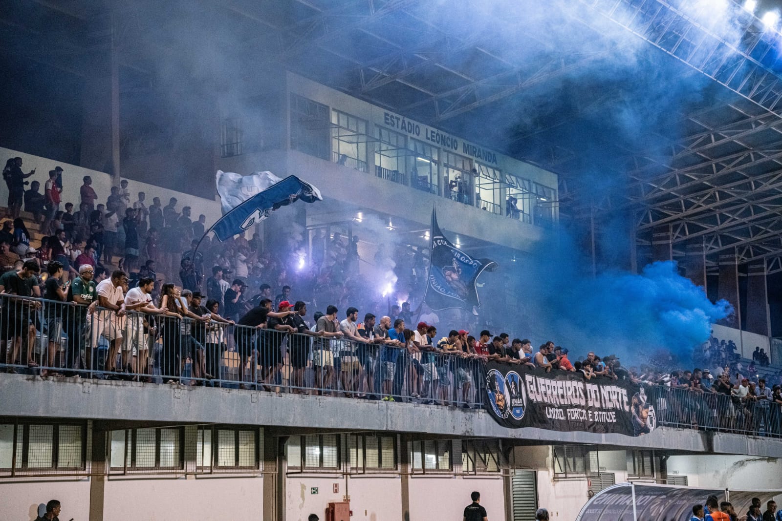 Guerreiros do Norte com faixa e sinalizadores azuis na arquibancada do Estádio Leôncio Miranda